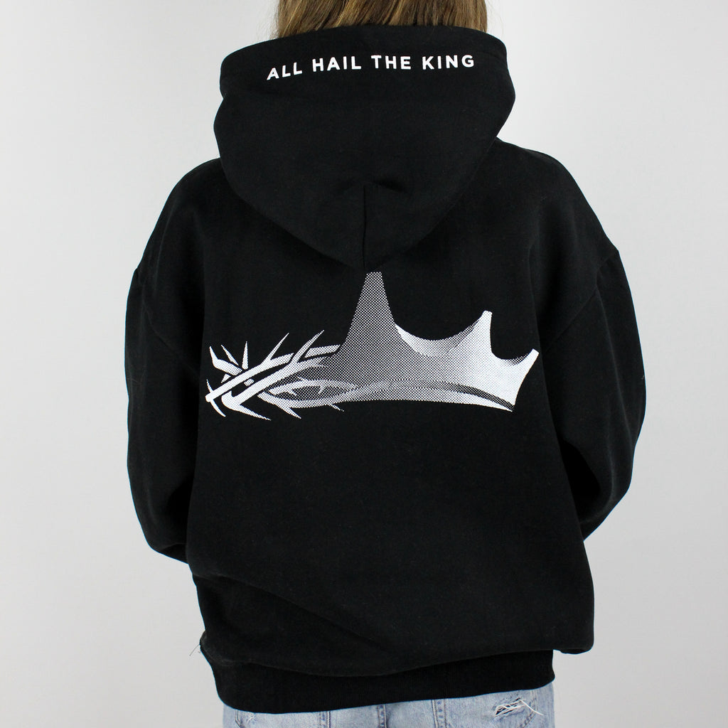 a model wearing a king Jesus oversized hoodie in black. The back design features a crown design that is half a crown of thorns and half a regular crown. There is also text saying "all hail The King".