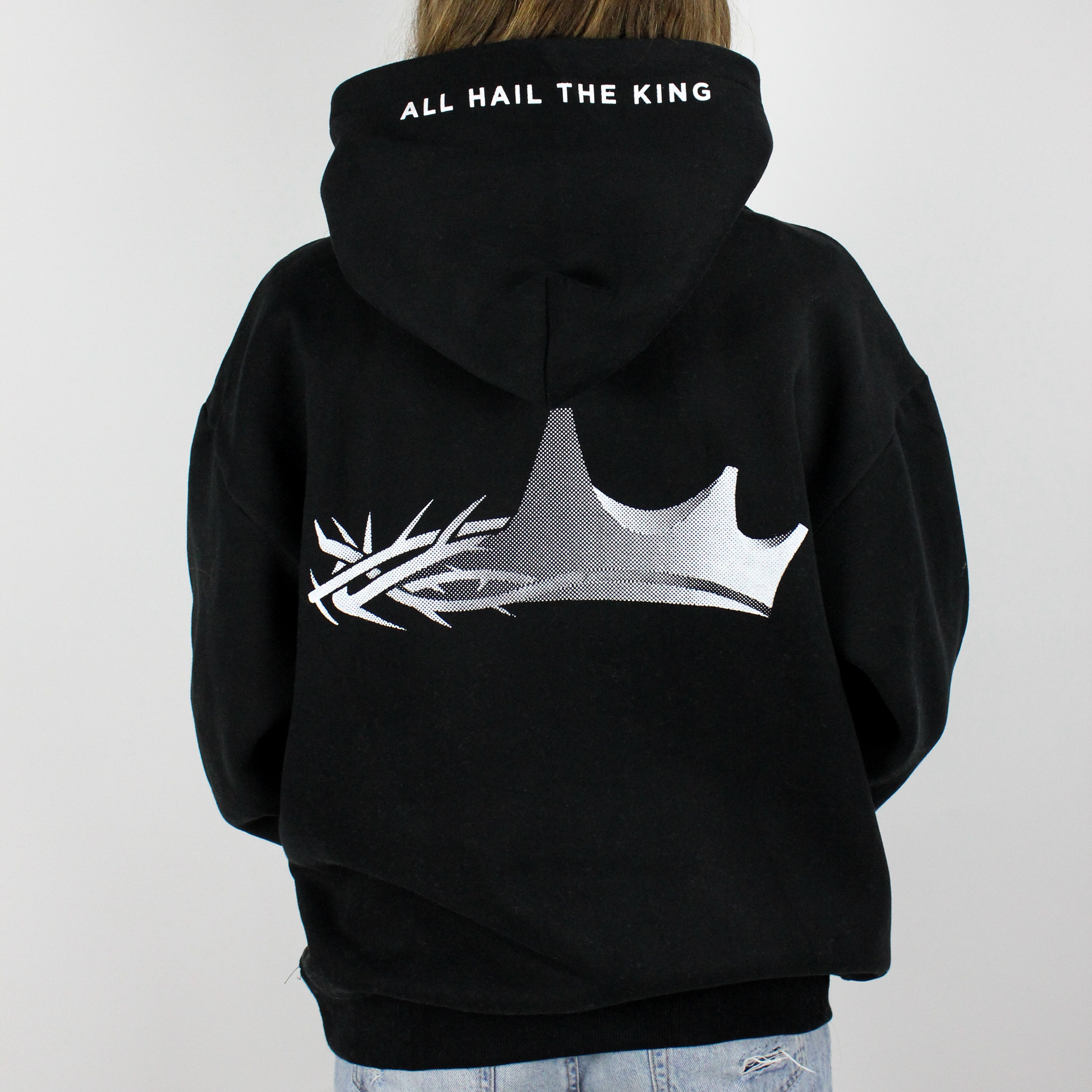a model wearing a king Jesus oversized hoodie in black. The back design features a crown design that is half a crown of thorns and half a regular crown. There is also text saying "all hail The King".