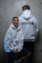 Load image into Gallery viewer, Two models wearing light gray hoodies from the back and front, standing against a textured gray concrete wall. The model in the back wears a large black graphic of a crown and branch on the back, while the model in the front wears a small black logo on the left chest.
